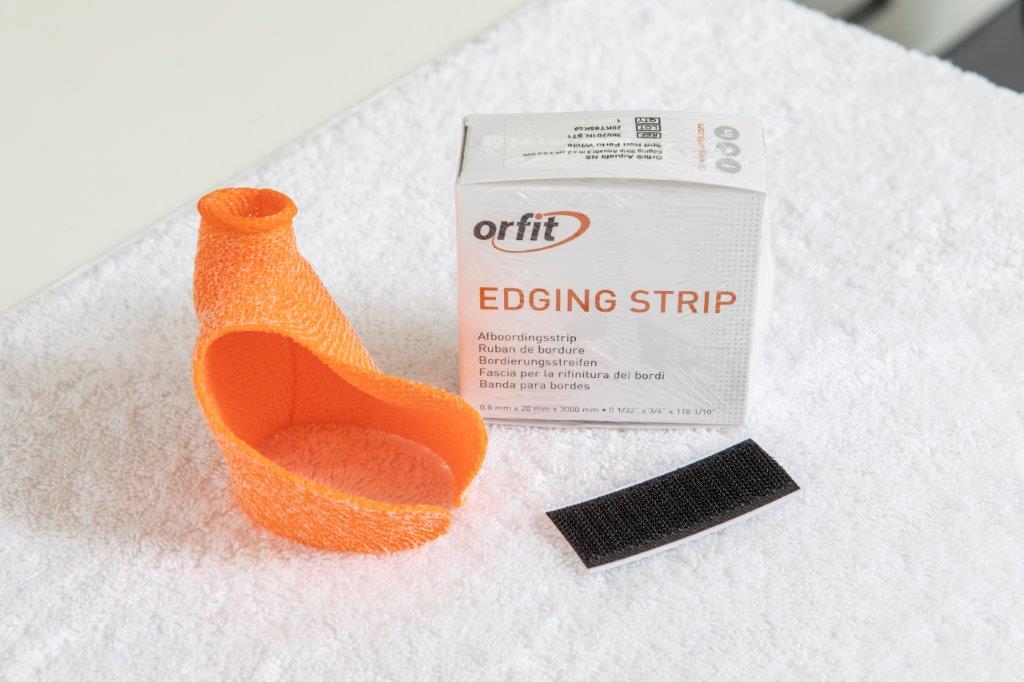Orficast orange orthosis, a box of edging strip and a piece of hook tape