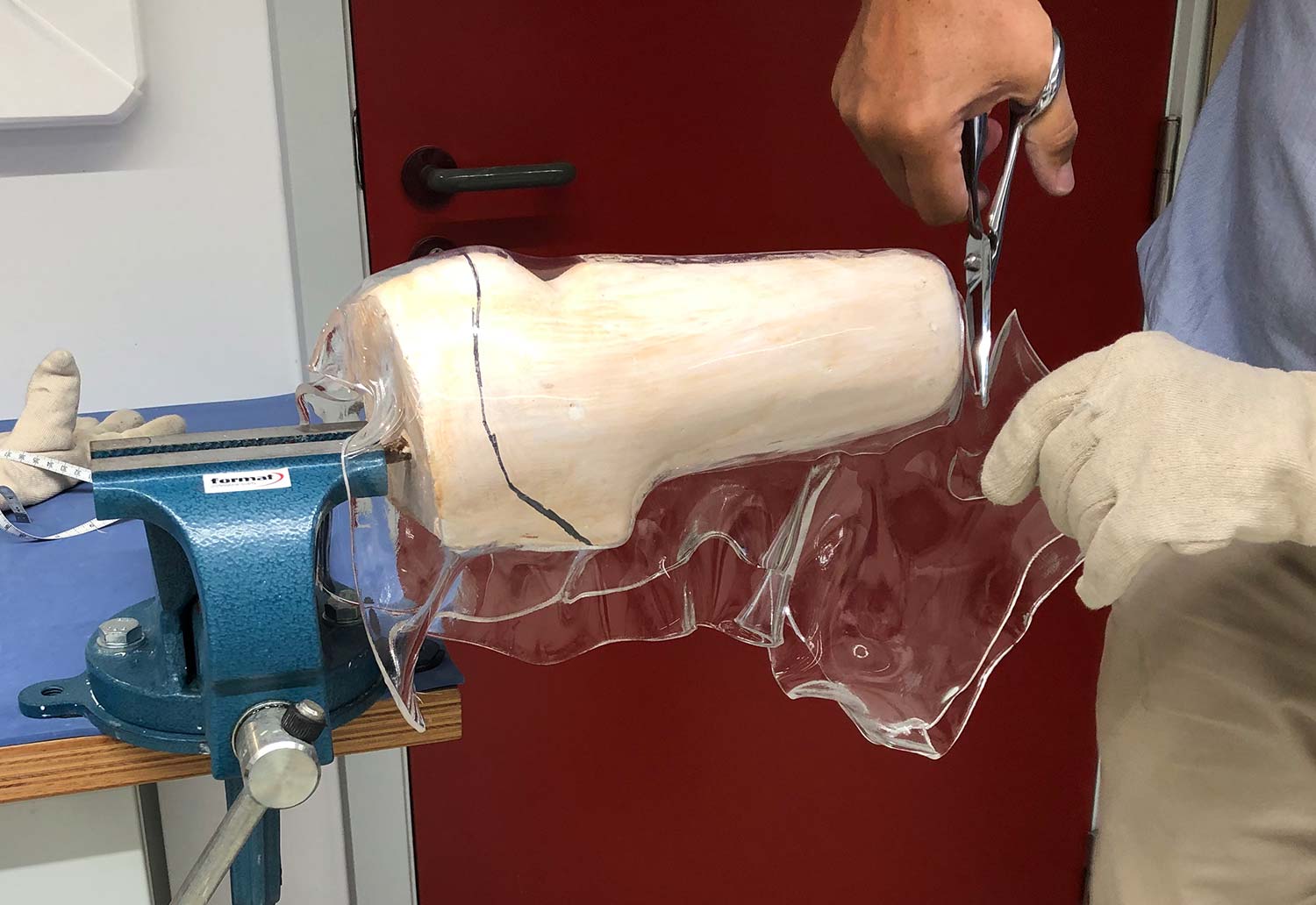 Man using scissors to trim a drape formed thermoplastic transtibial socket.